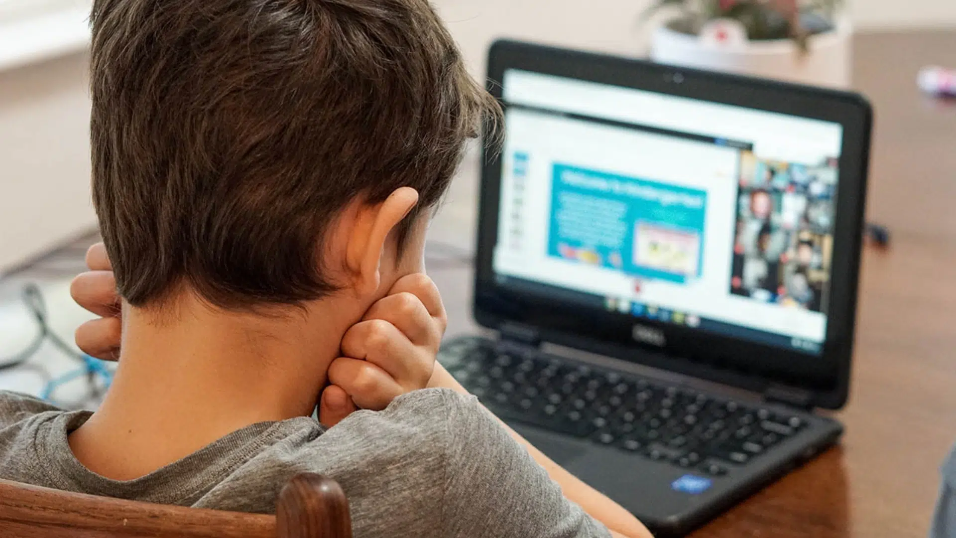 a child sits at a table using a chromebook for an online class appearing frustrated and thinking why is my chromebook so slow