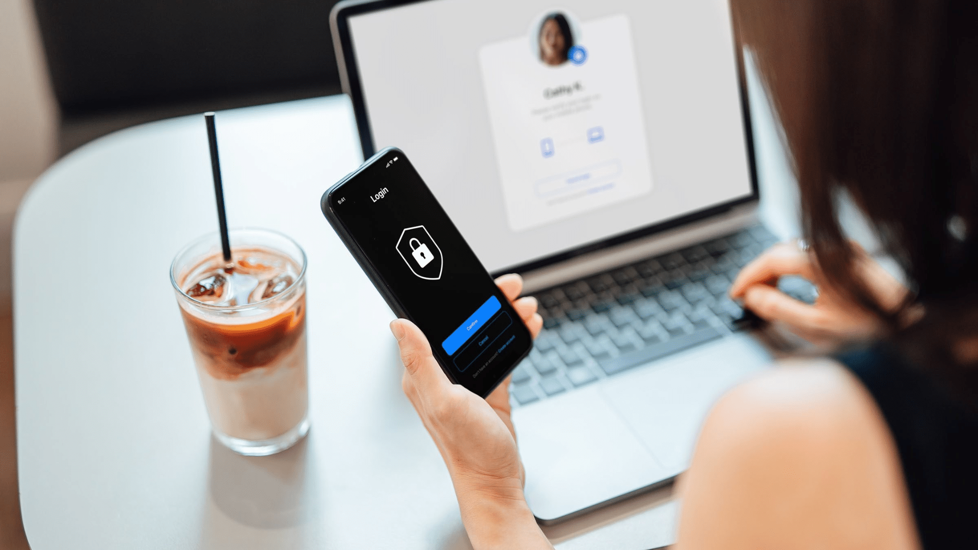 a person logs into an account on their phone using public wi-fi with a laptop and iced coffee nearby