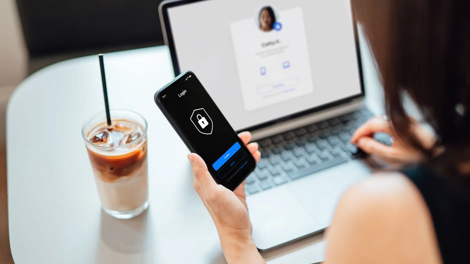 a person logs into an account on their phone using public wi-fi with a laptop and iced coffee nearby