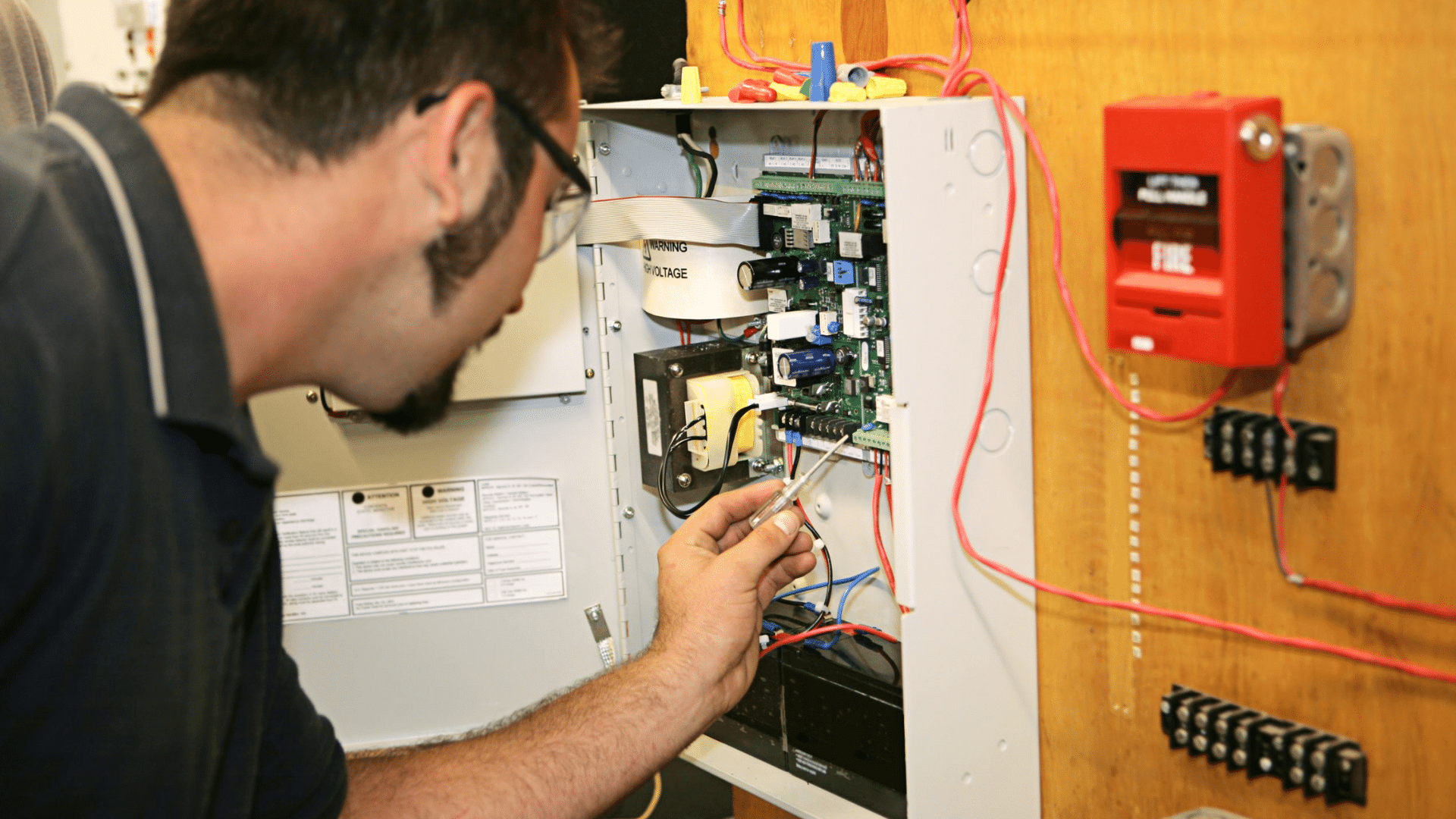 _technician inspecting an open control panel during fire alarm maintenance and fire alarm repair work featured image
