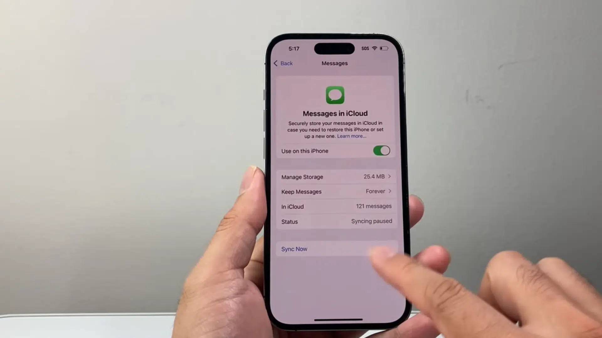 a hand holding an iphone showing messages in icloud settings while tapping the sync now option on screen