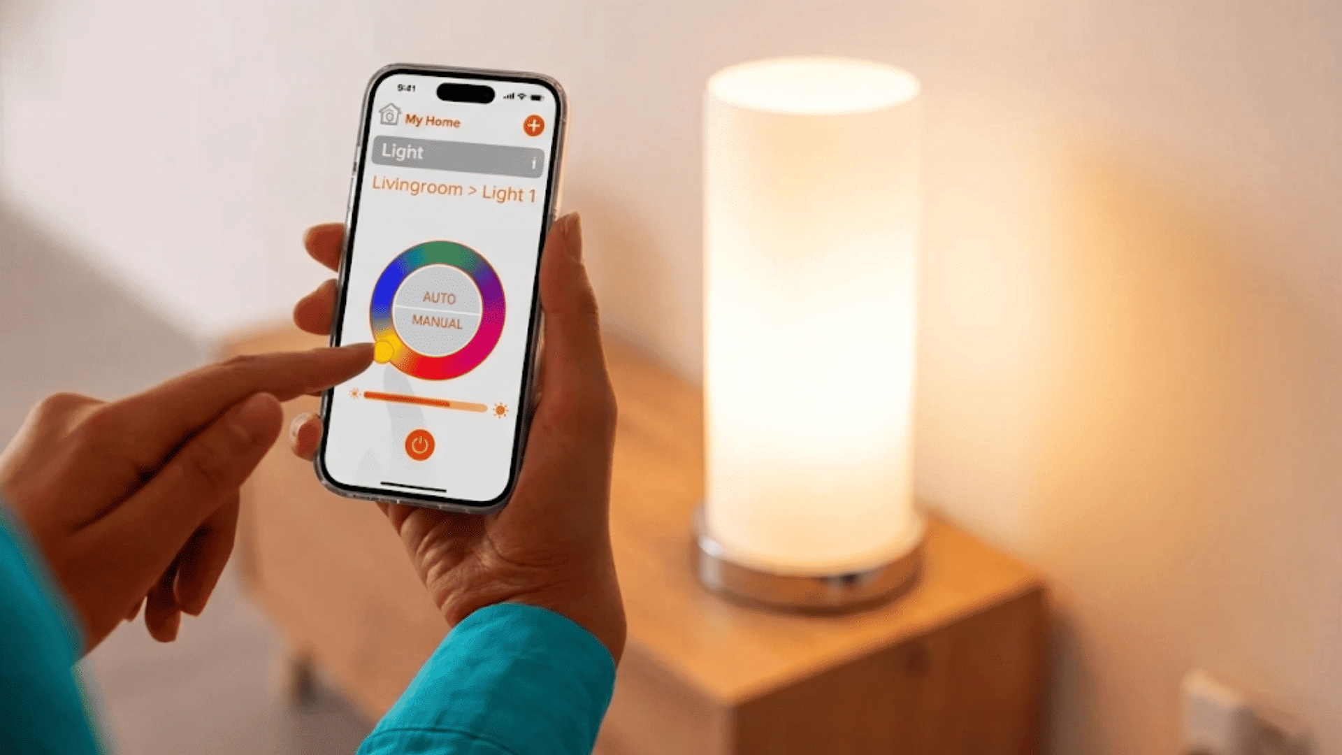person using a smartphone app to adjust brightness and color settings of a glowing smart table lamp indoors