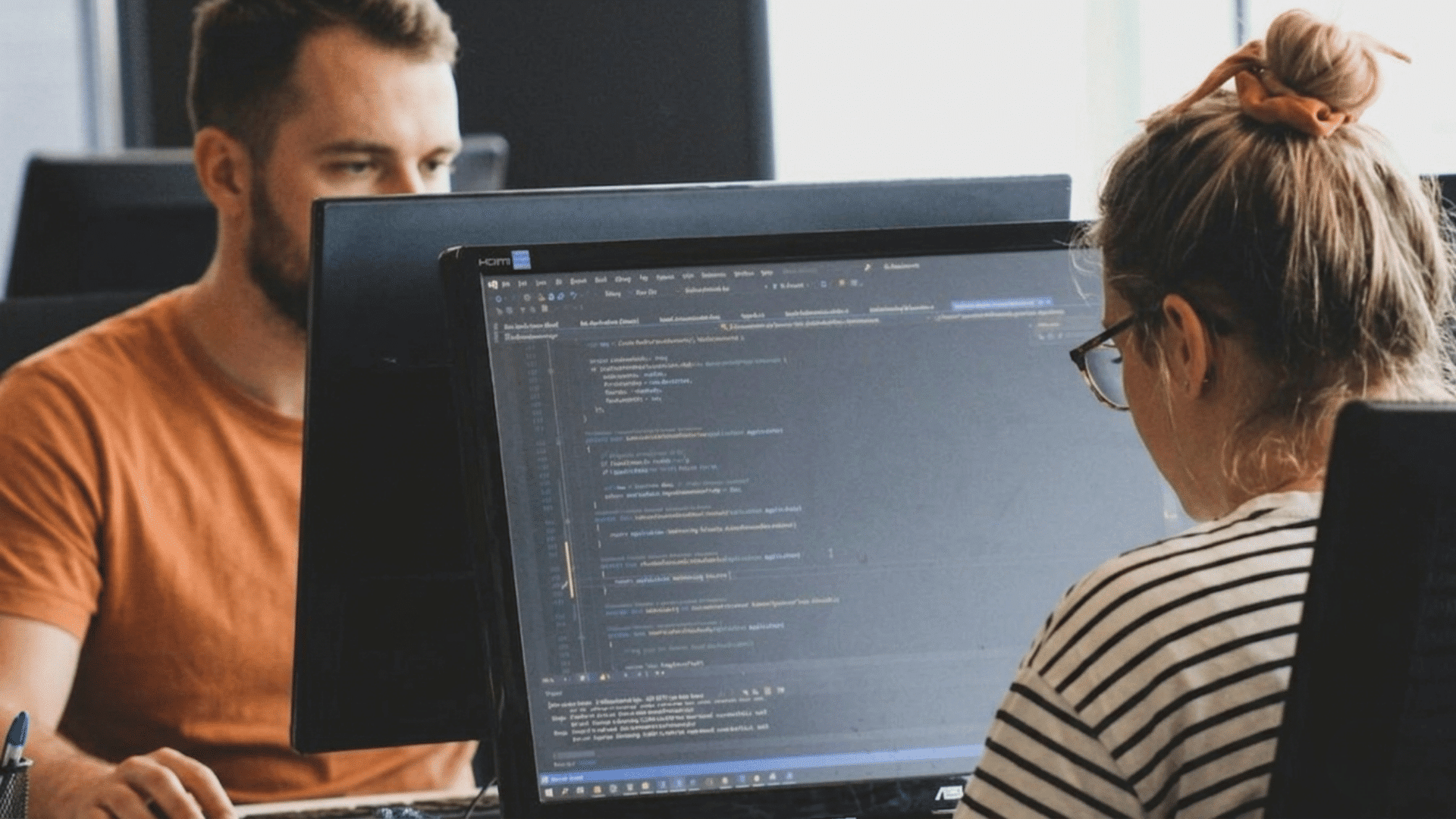 software developers working at desktop computers while reviewing code in a shared office space