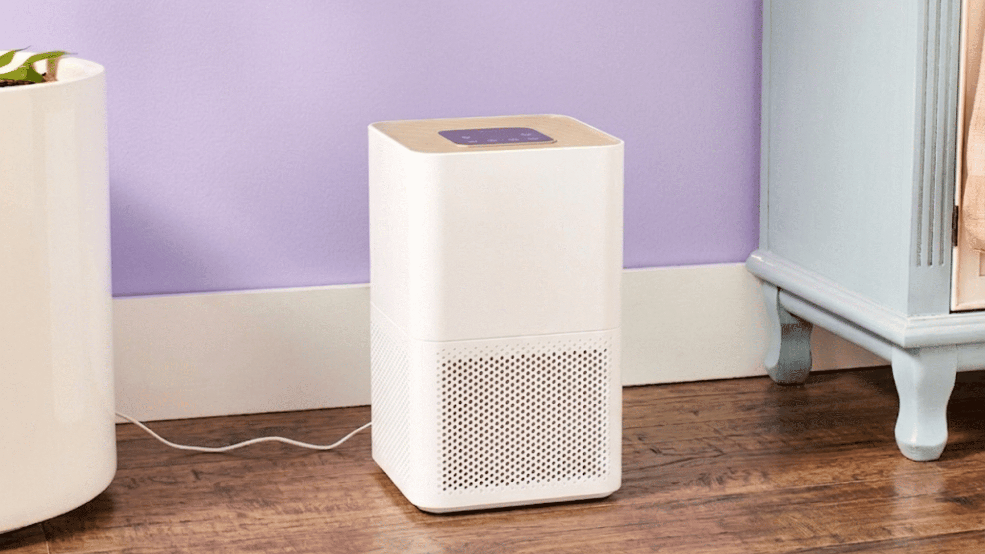 white levoit air purifier placed on a wooden floor beside furniture against a light purple wall indoors