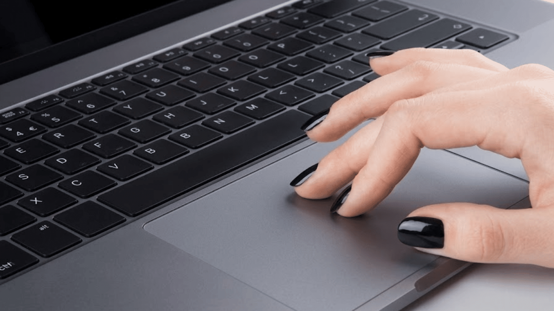 hand with black painted nails using the touchpad on a laptop keyboard viewed from a close angled perspective