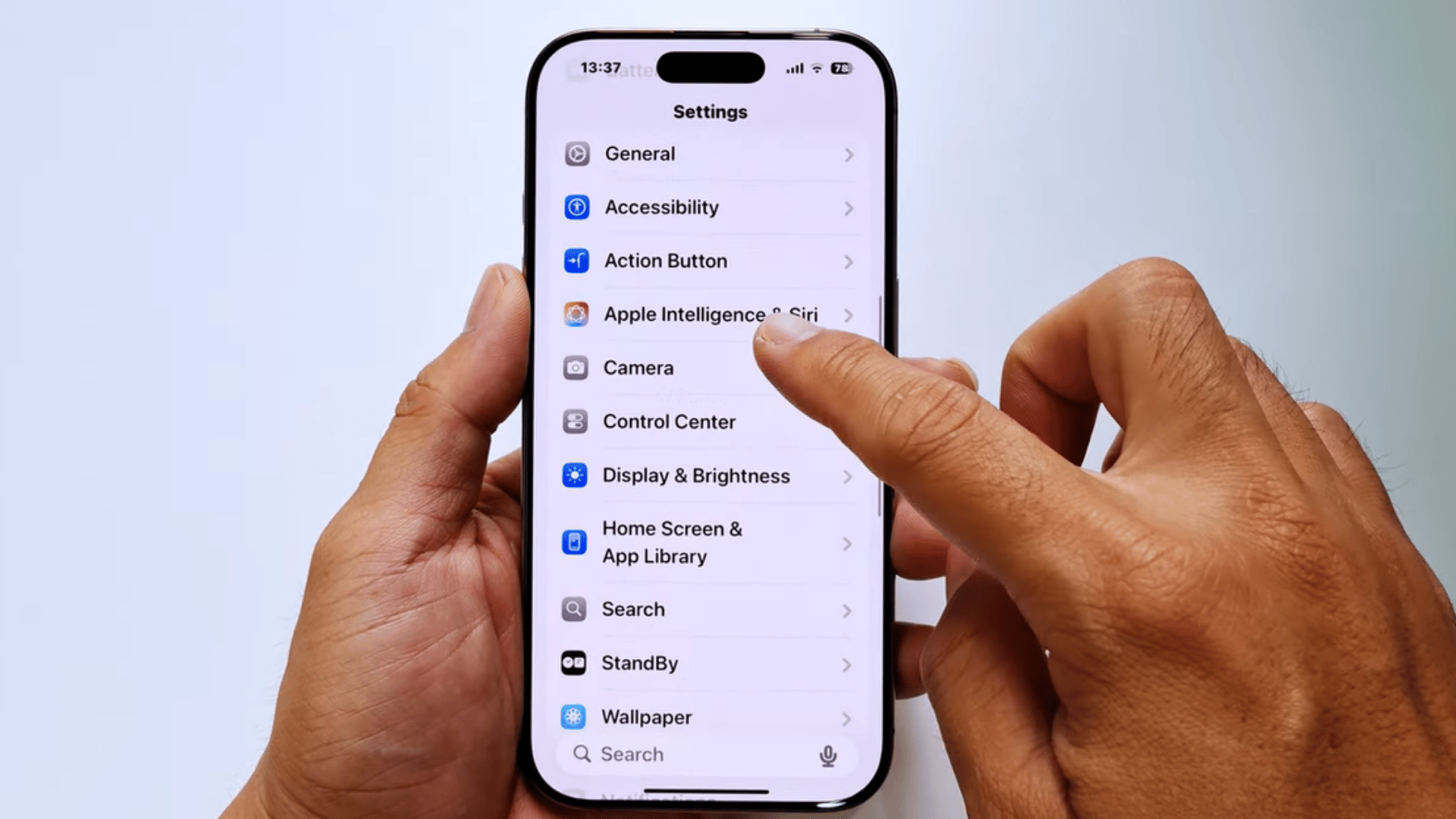 hands holding an iphone displaying the settings menu while a finger taps apple intelligence and siri options