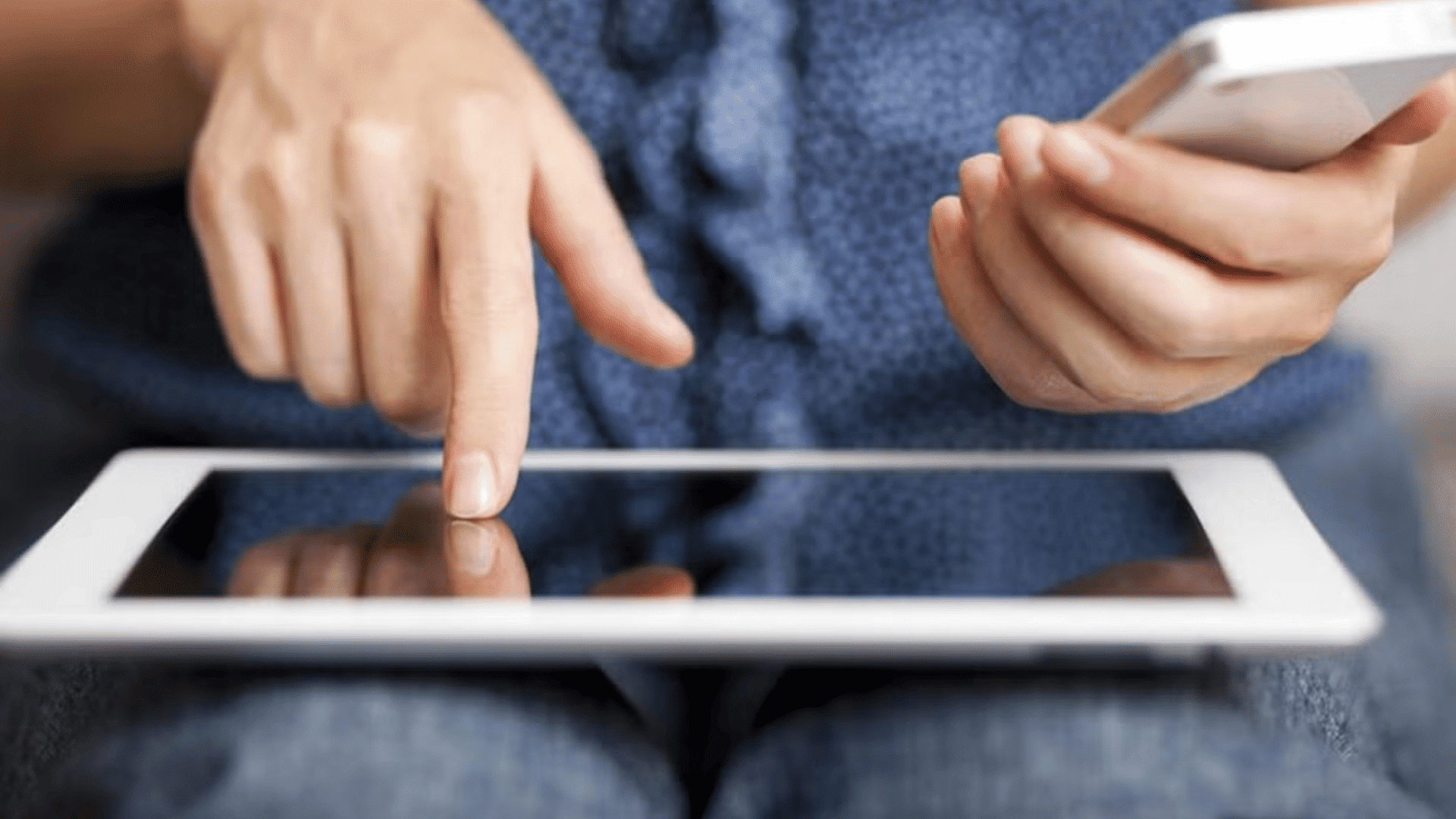 person holding a smartphone while tapping a tablet screen and using multiple mobile devices at the same time