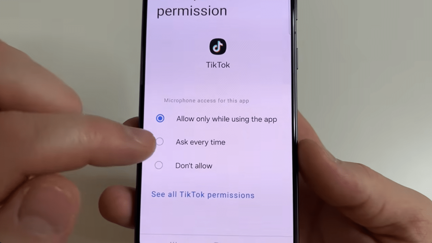 hand adjusting smartphone settings screen showing tiktok microphone permission options with allow only while using selected