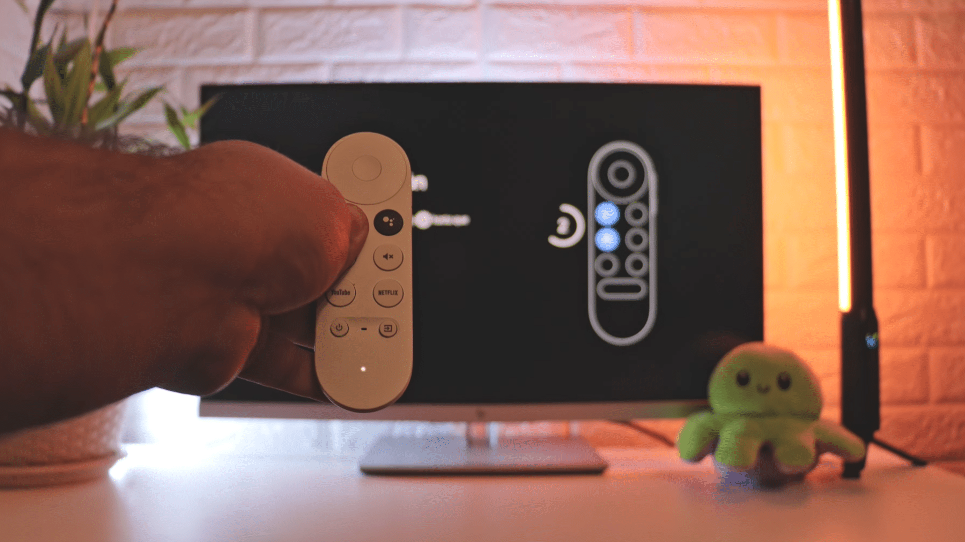hand holding a remote control aimed at a television screen showing remote setup interface in a softly lit room
