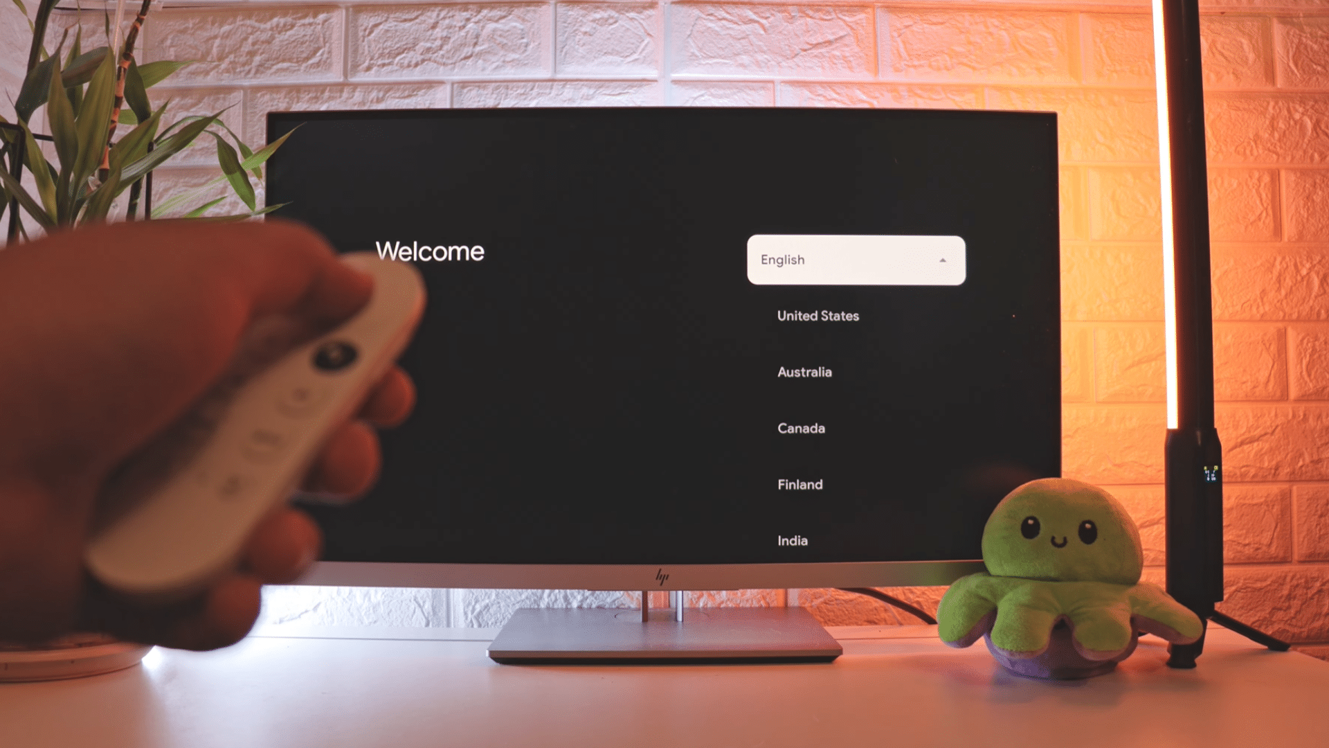 hand holding a remote control while selecting language and region options on a television welcome setup screen in a cozy room