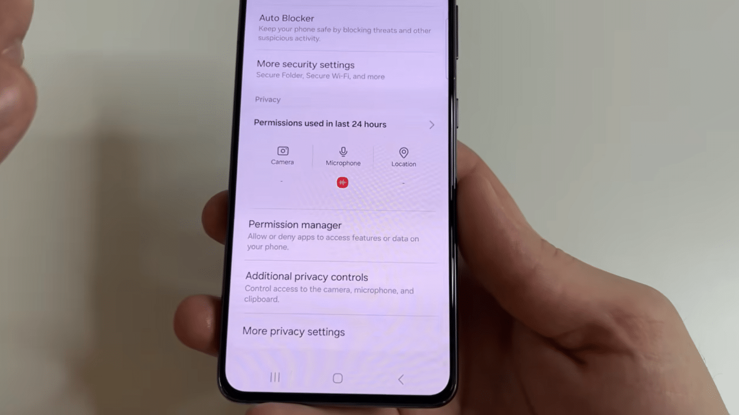_hand holding smartphone on privacy settings screen showing permission manager and recent access for camera microphone and location