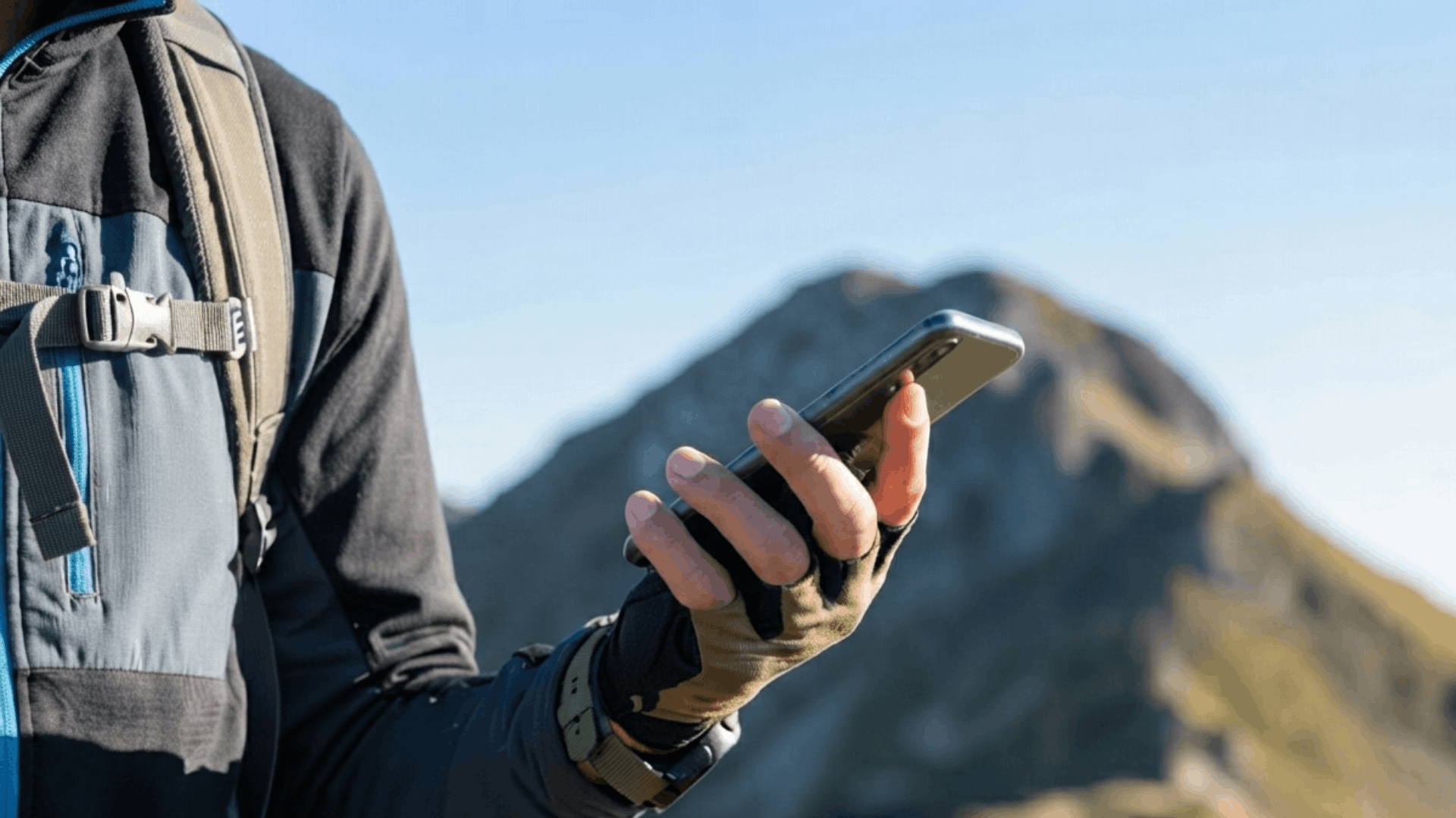 person using a smartphone outdoors with mountains in the background during a hiking adventure