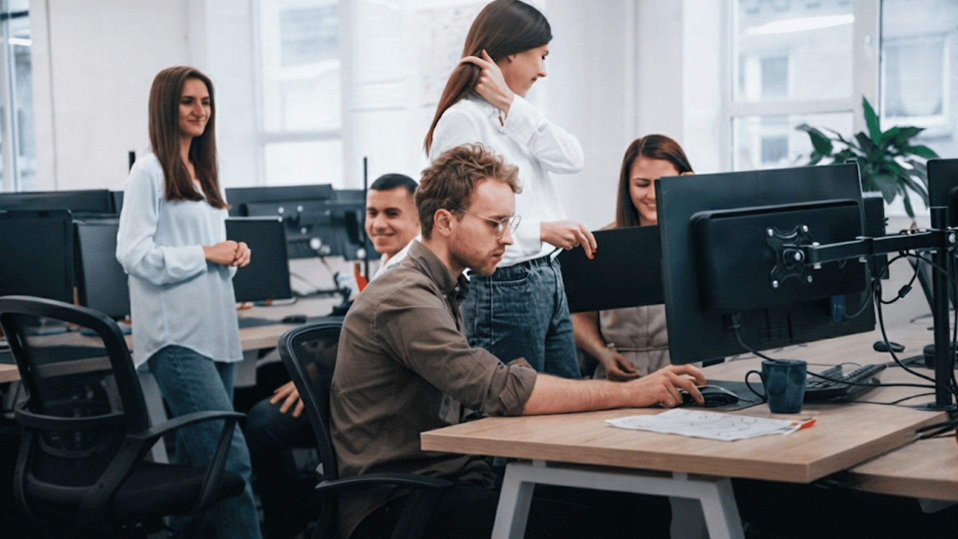 team members collaborating in a modern office while one person works at a computer and others gather around discussing a project