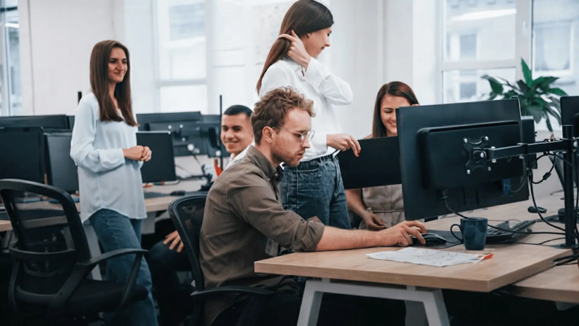 team members collaborating in a modern office while one person works at a computer and others gather around discussing a project