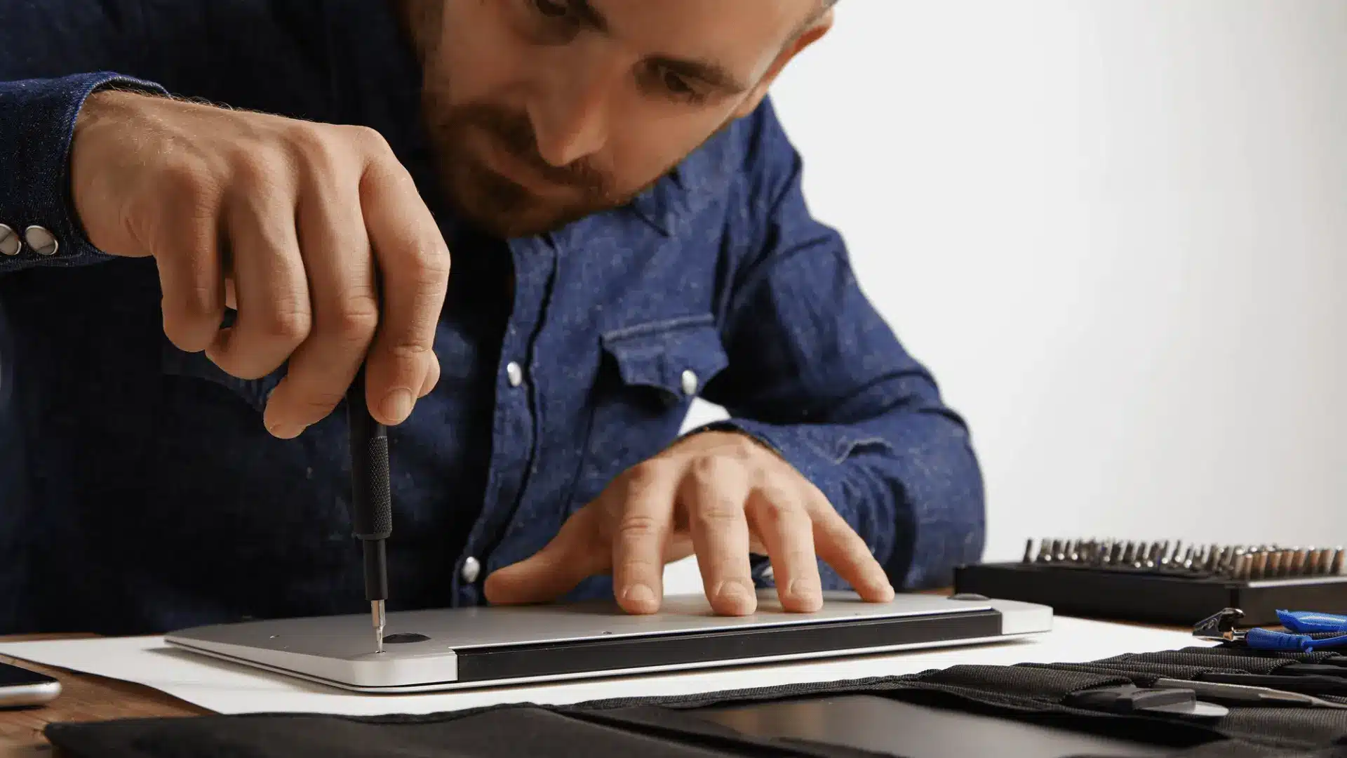 Technician using a screwdriver to open a laptop and inspect its internal hardware parts.
