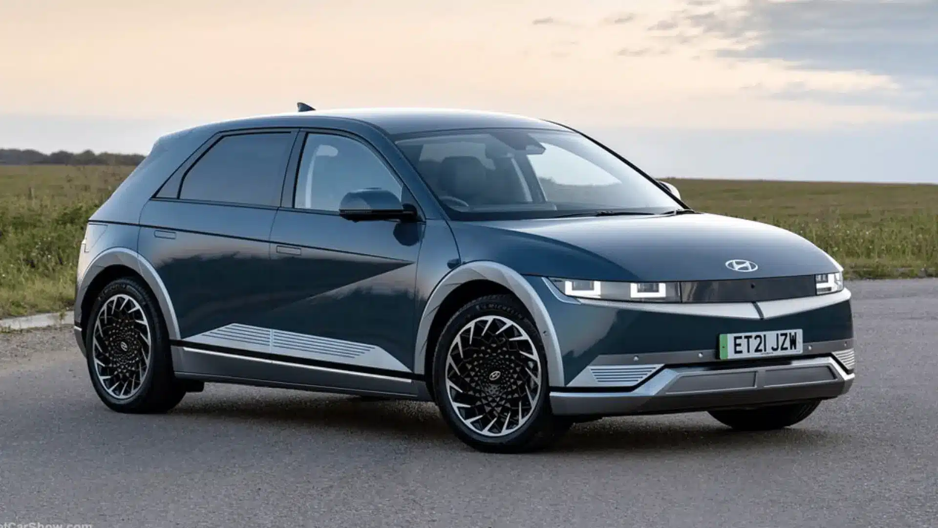 dark blue hyundai ioniq 5 electric car parked on a road with open fields and cloudy sky in the background