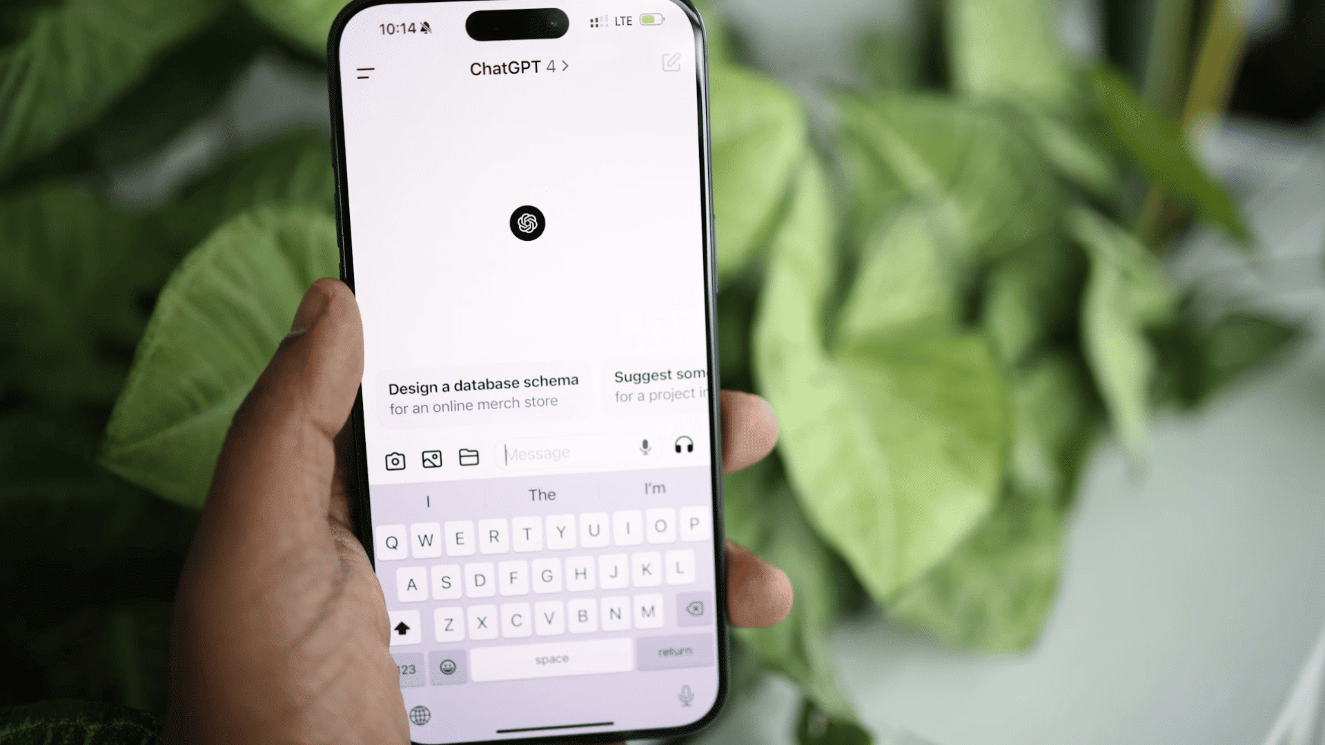 a hand holding a smartphone displaying the chatgpt app home screen with green plant leaves softly blurred in the background