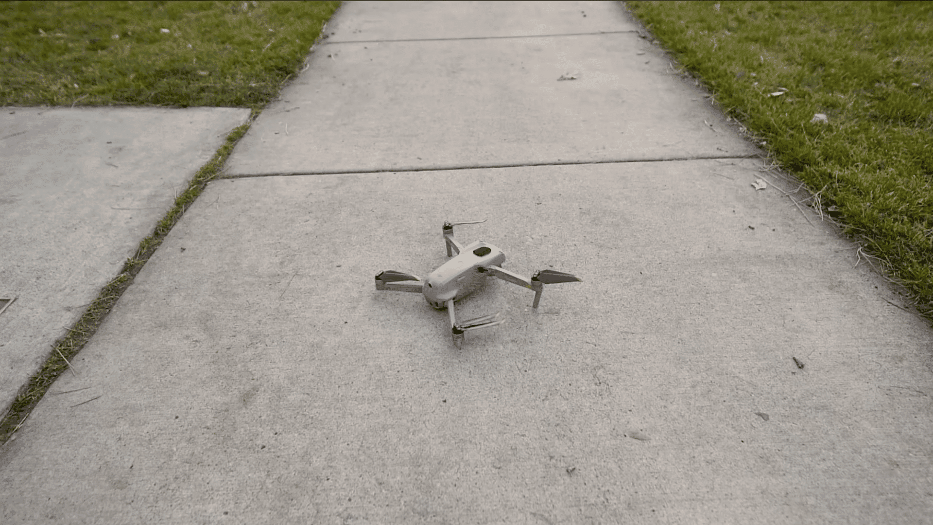small drone resting on a concrete sidewalk beside grass before a beginner practice flight