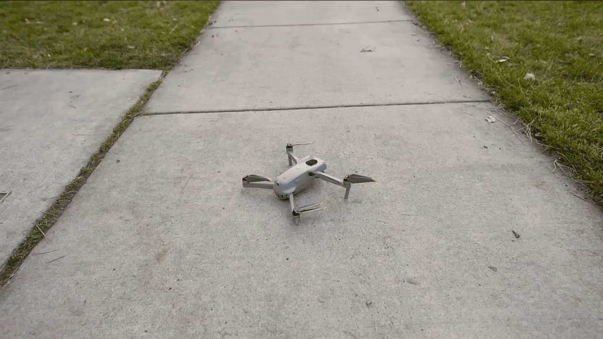 small drone resting on a concrete sidewalk beside grass before a beginner practice flight
