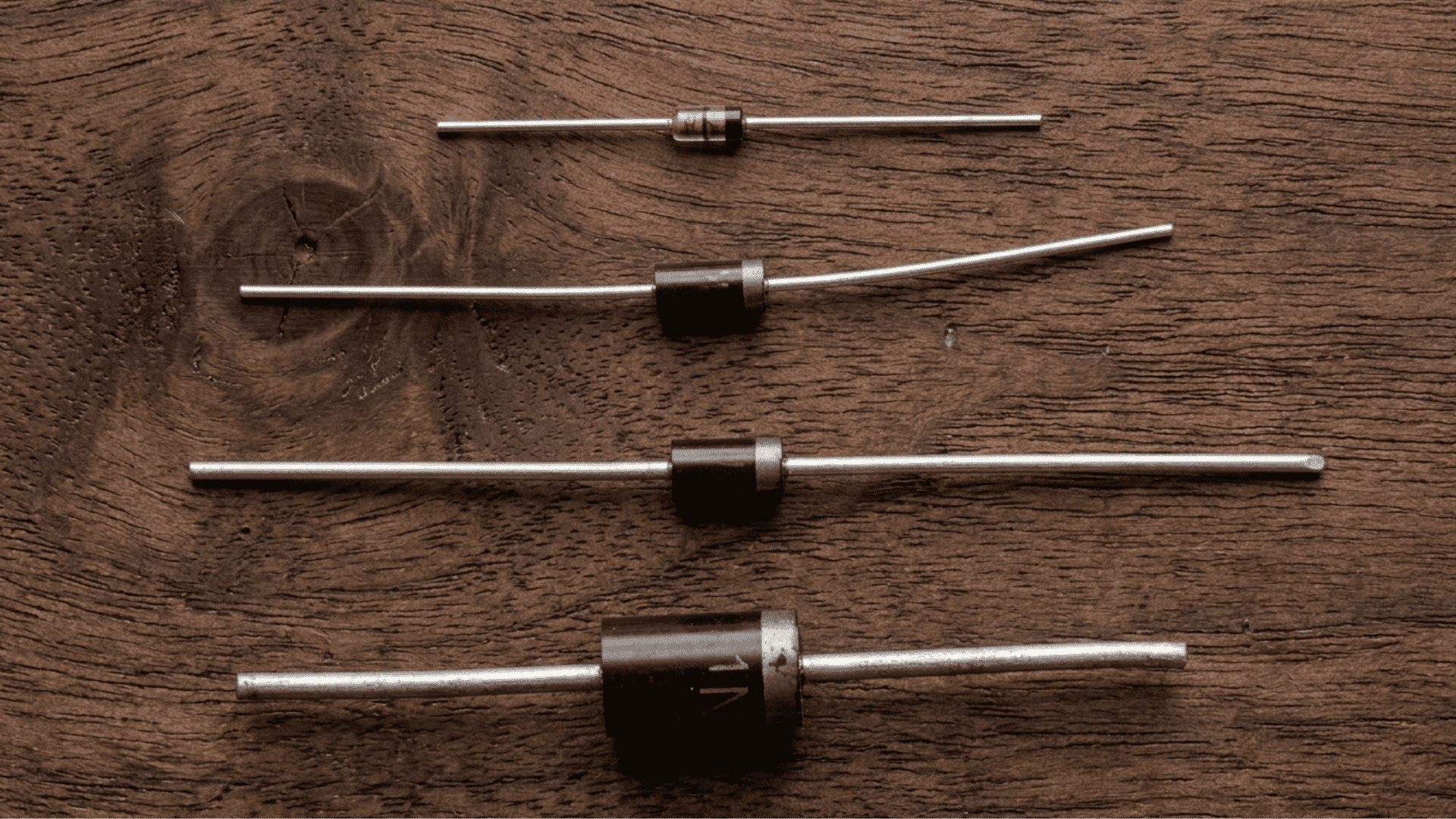Four semiconductor diodes of different sizes arranged on a wooden surface.