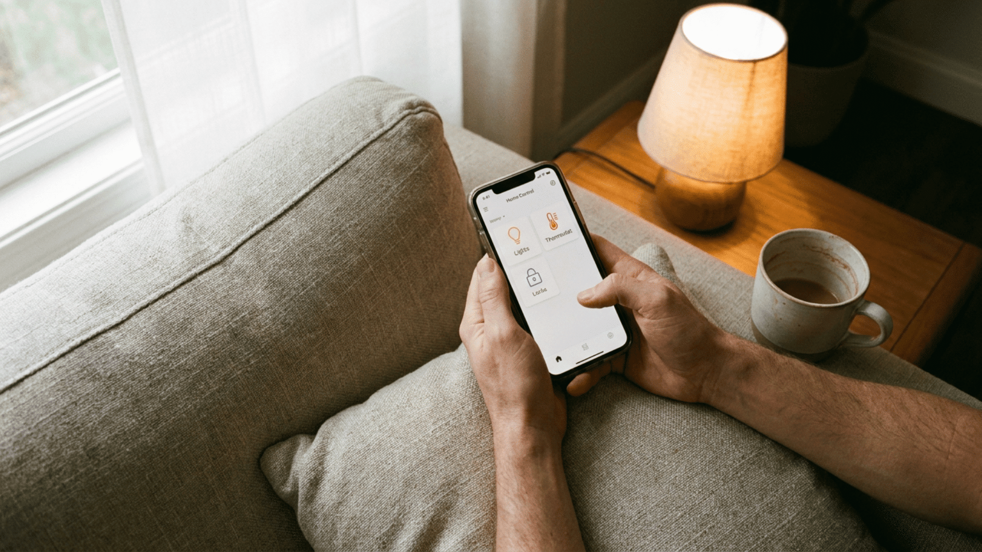 hands holding a phone with a home control app open on a linen sofa