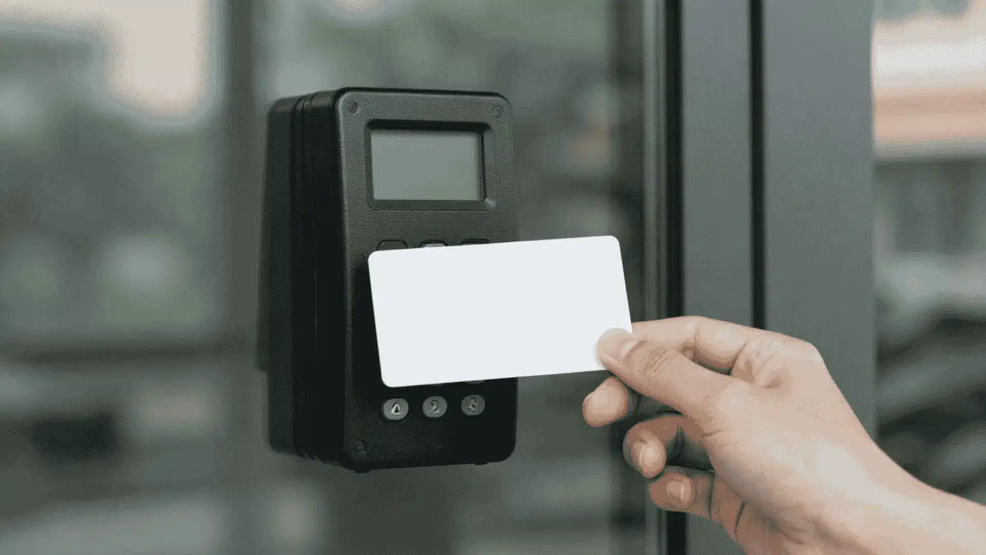 hand holding an rfid access card near a wall mounted reader beside a glass entry door