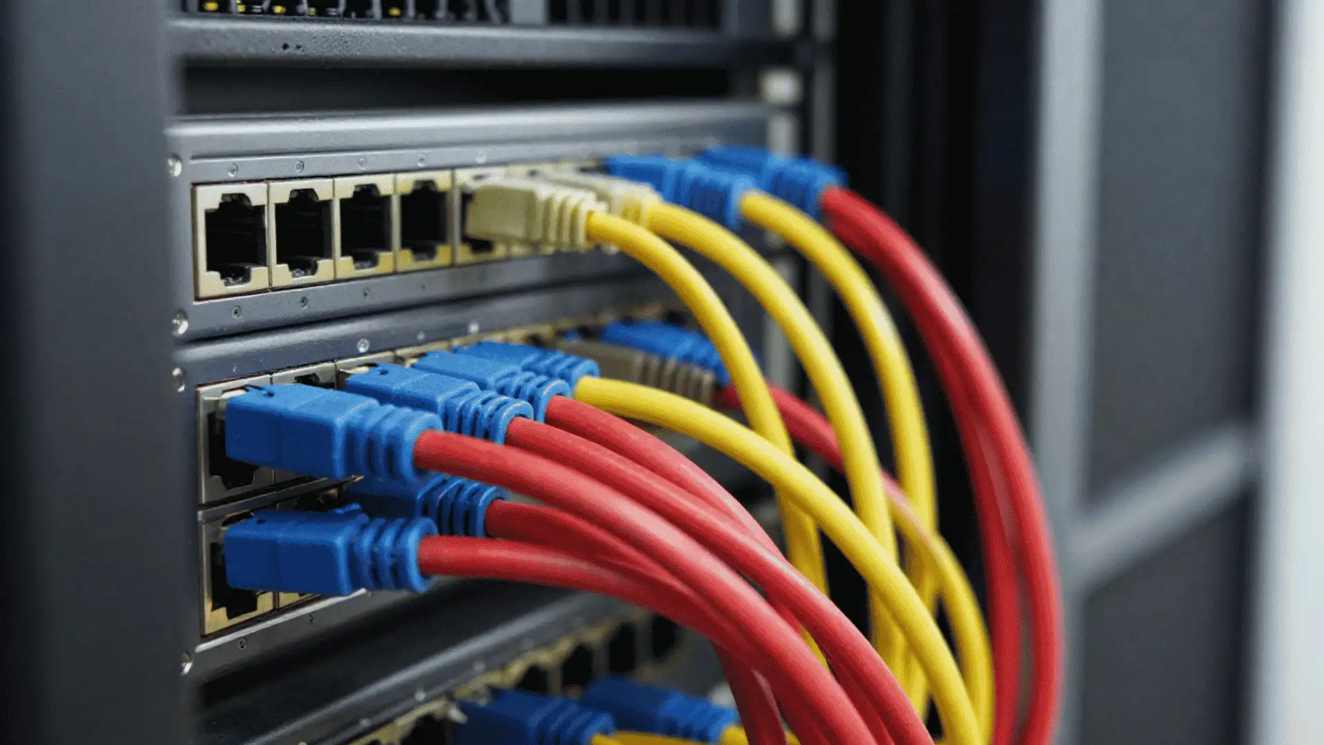 red yellow and blue networking cables plugged into multiple ports on a server rack system