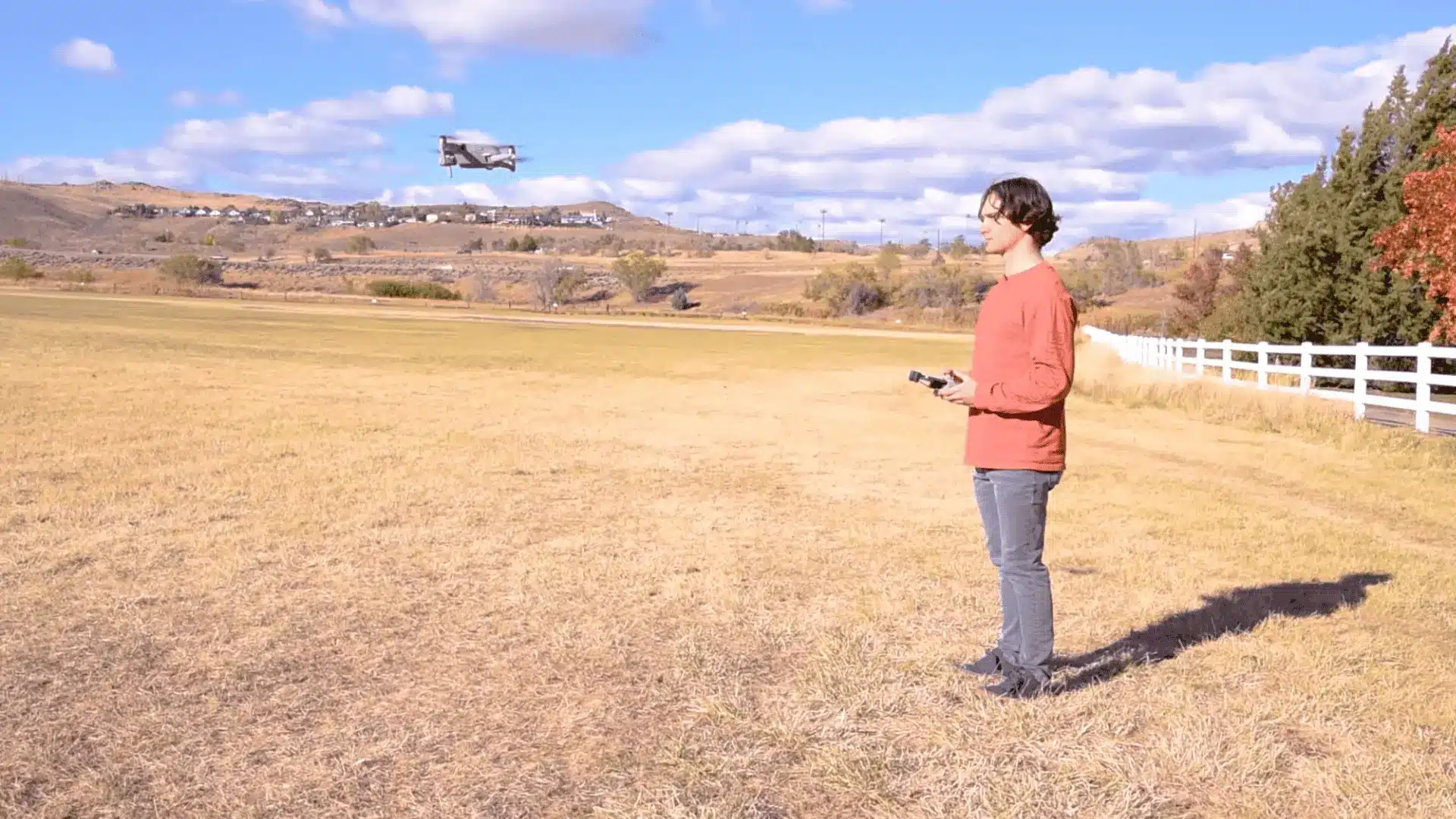 person holding a controller while a drone hovers at low height over an open grassy field