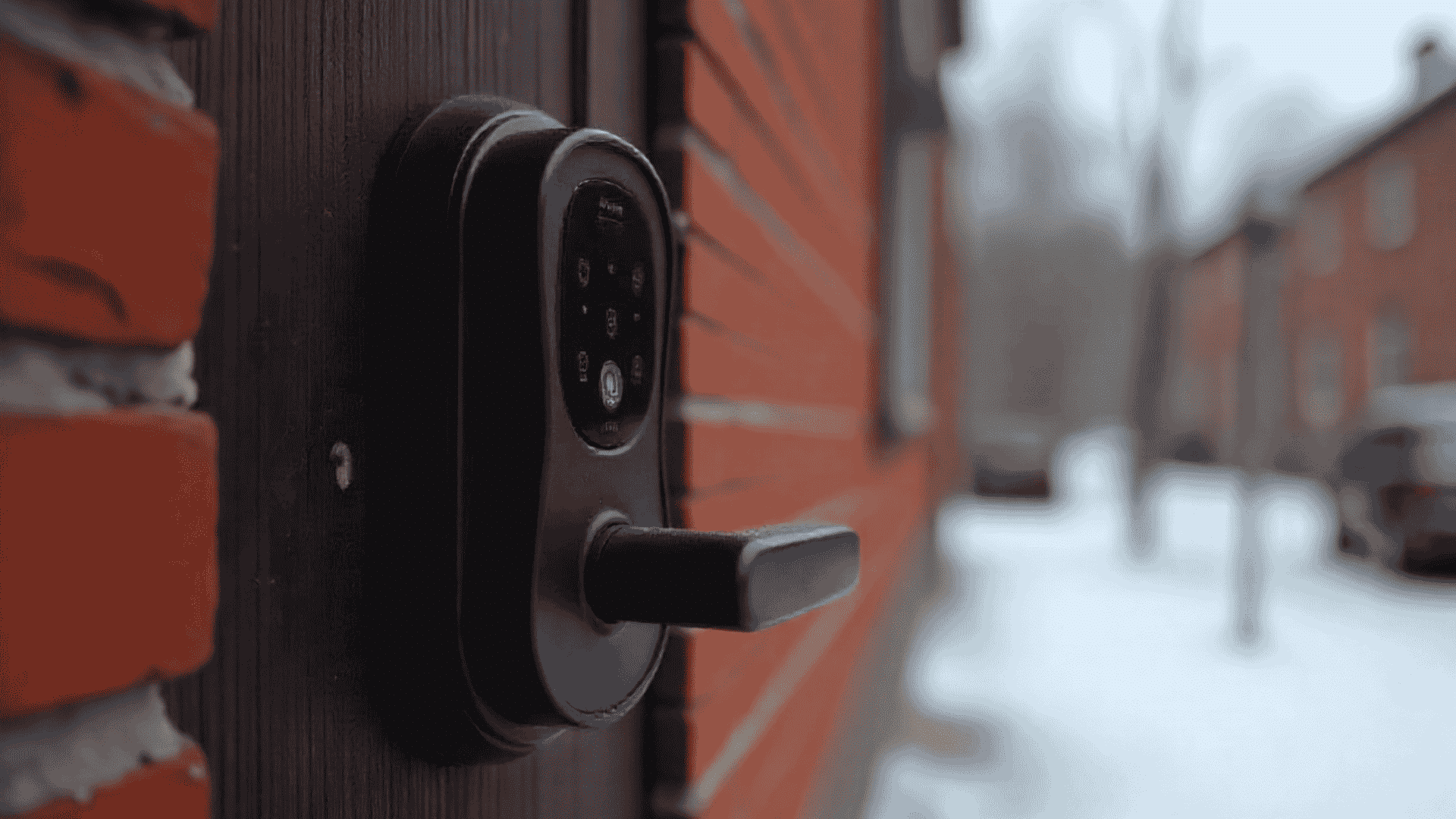 smart lock with a keypad is mounted on a red brick wall next to a wooden door background shows a snowy street