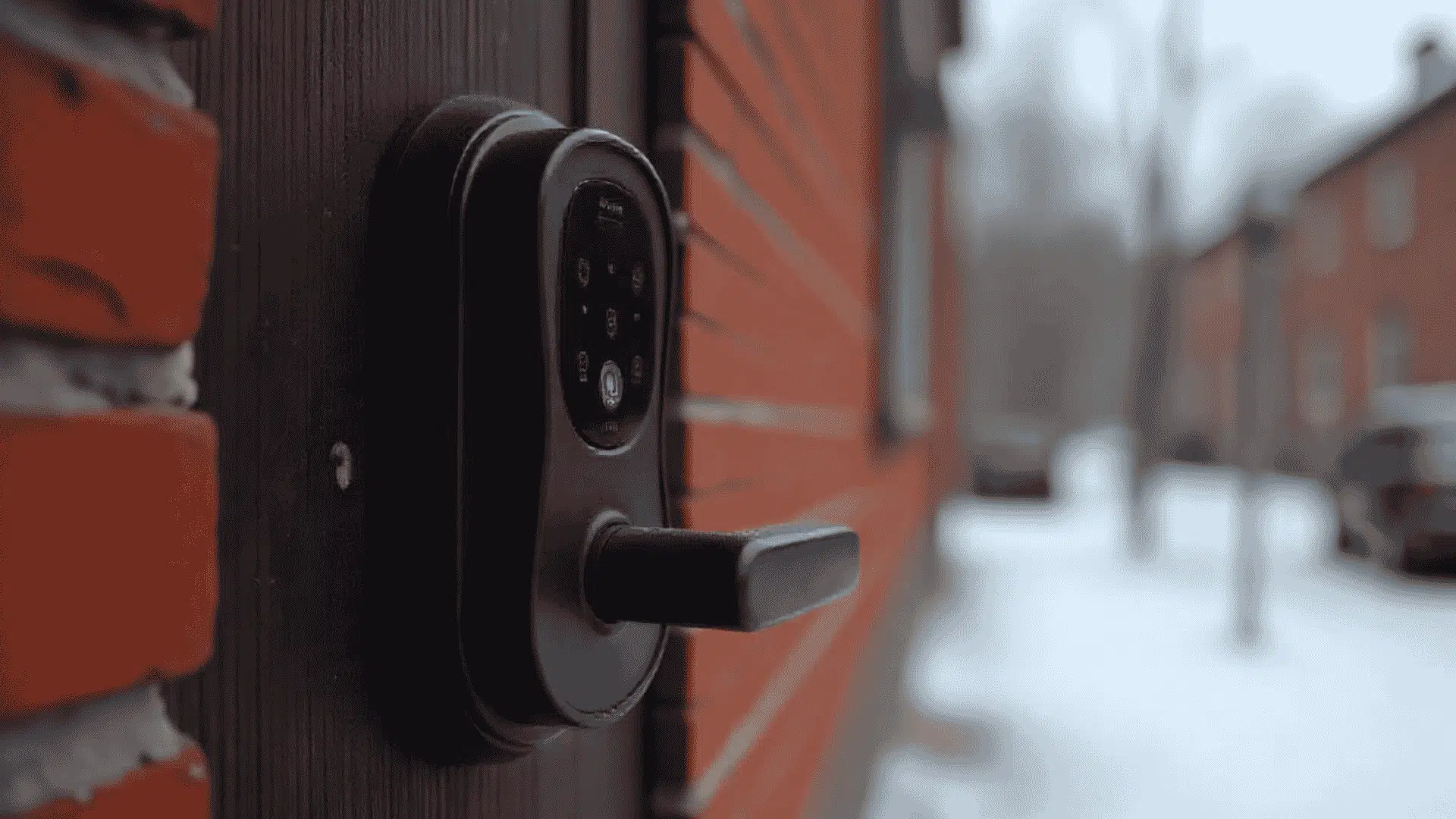 smart lock with a keypad is mounted on a red brick wall next to a wooden door background shows a snowy street