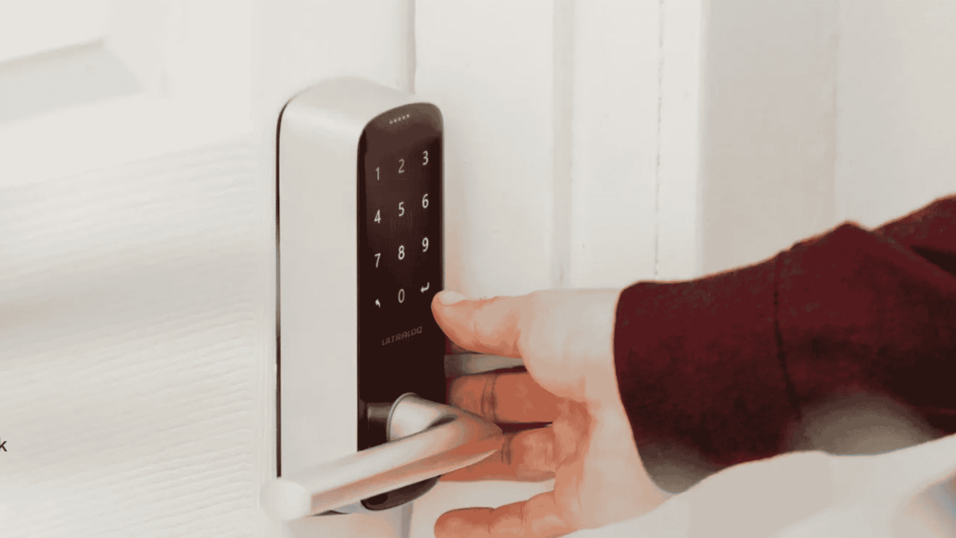 person opening a white door using a silver ultraloq keypad smart lock with lever handle
