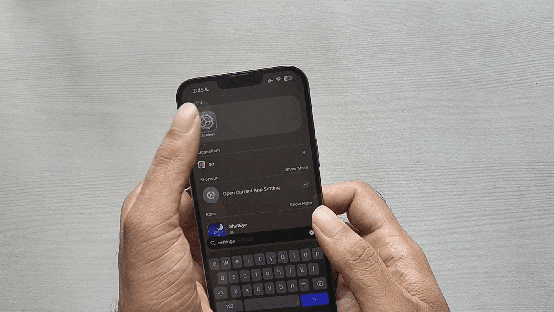 person holding a smartphone with settings search open showing app suggestions and keyboard on the screen