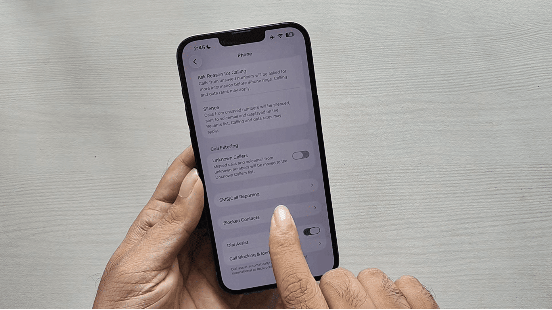 person viewing iphone phone settings with blocked contacts option visible and finger pointing at the call settings menu