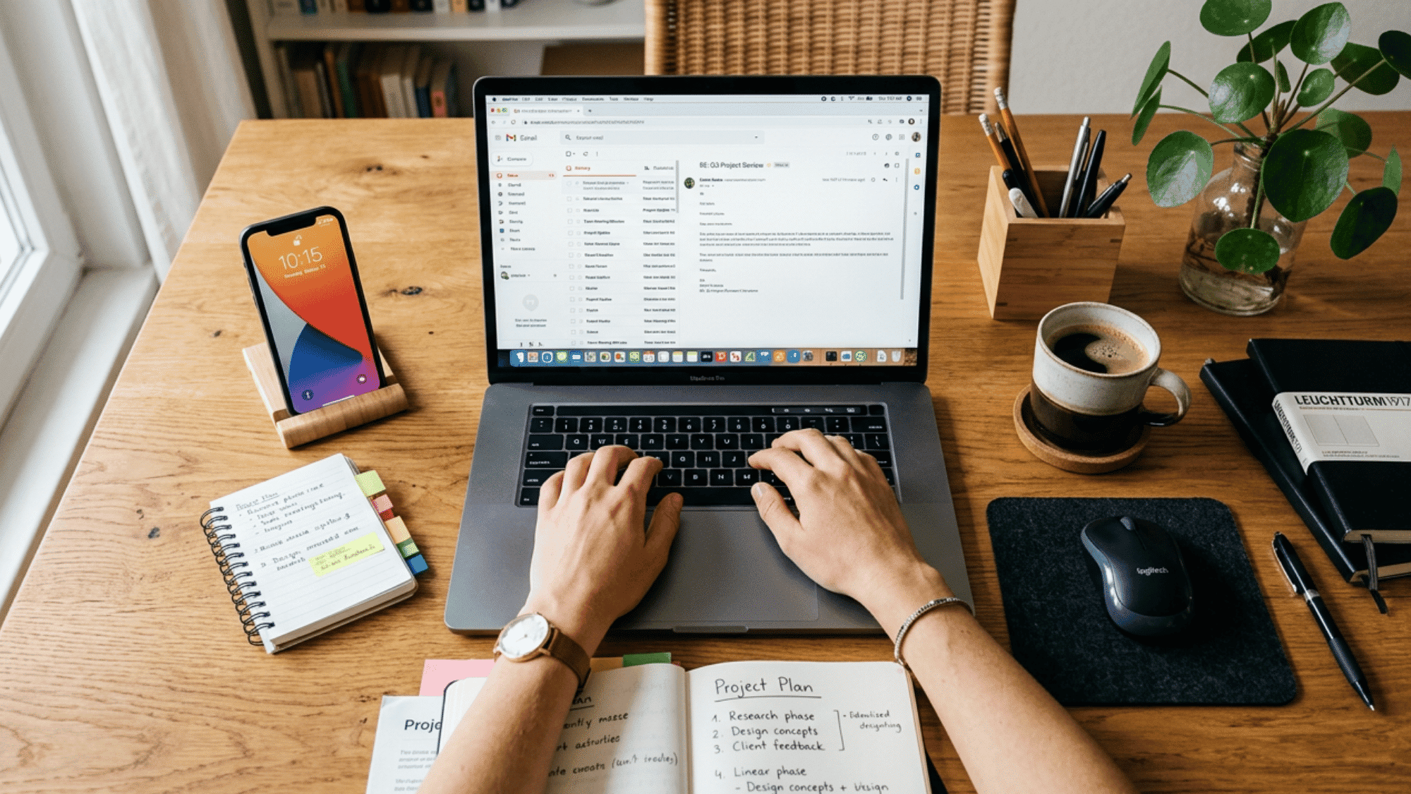 person working on a laptop at a wooden desk with smartphone notebook coffee and office supplies at home