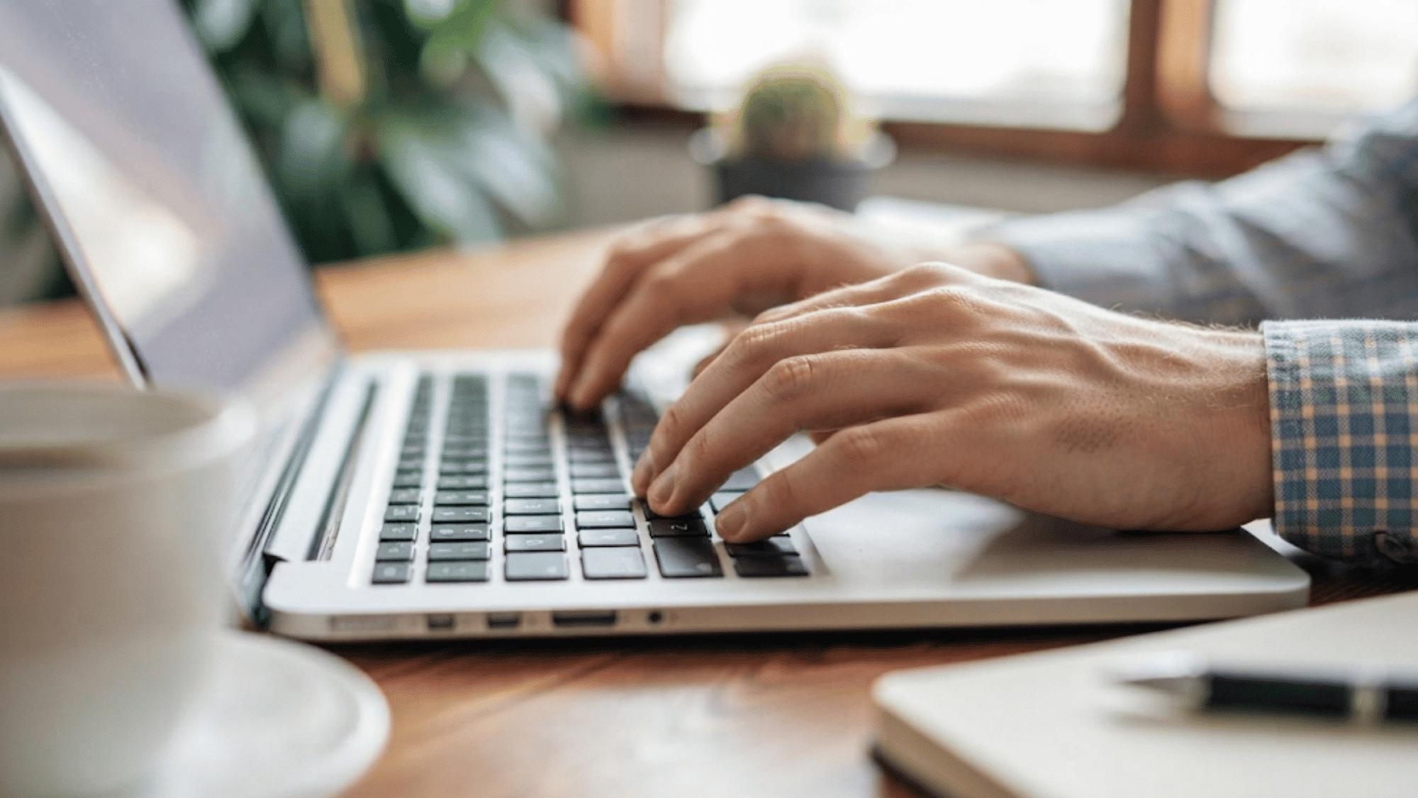 hands typing on a laptop keyboard while working at a desk in a modern home office setting