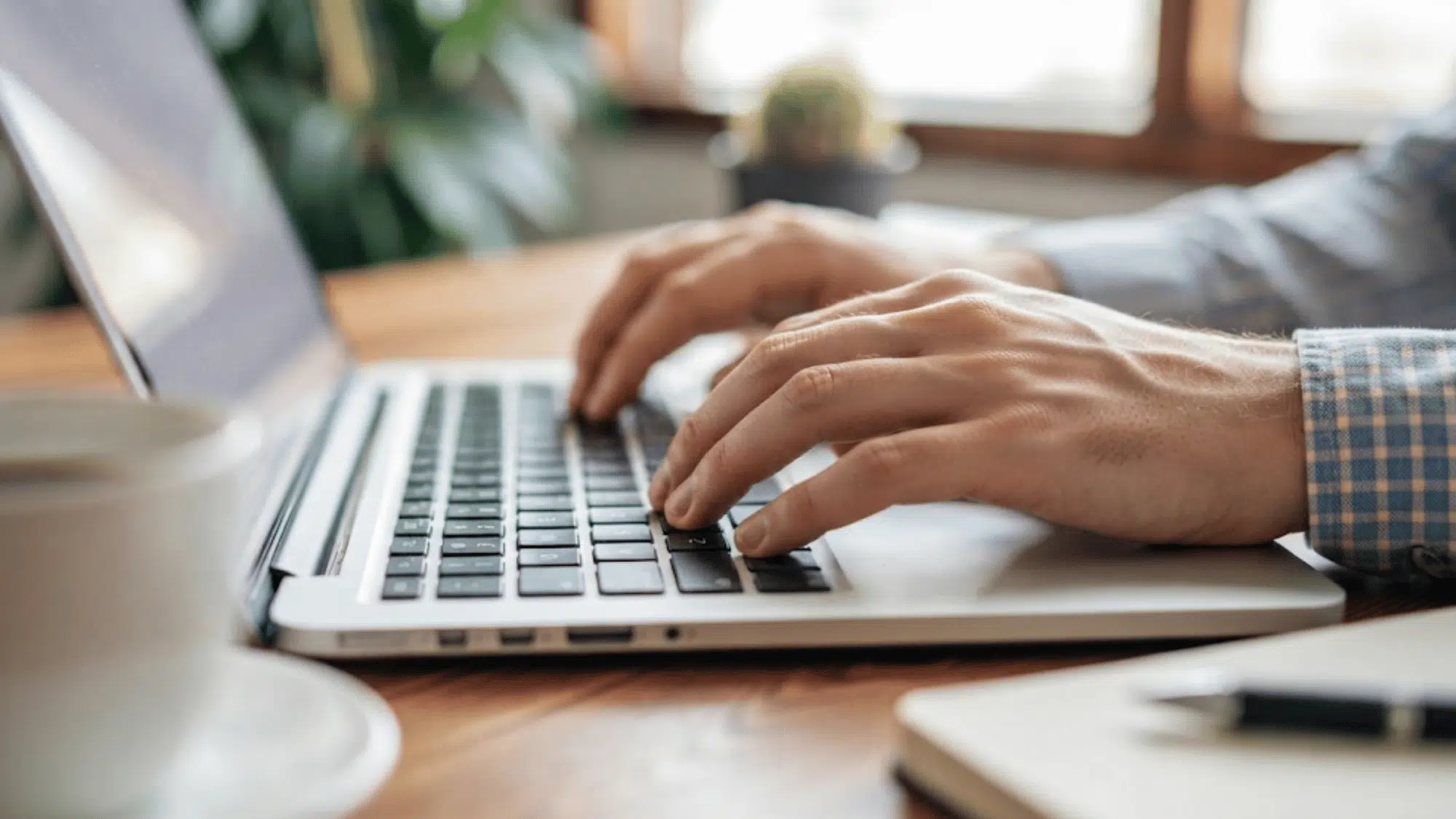 hands typing on a laptop keyboard while working at a desk in a modern home office setting